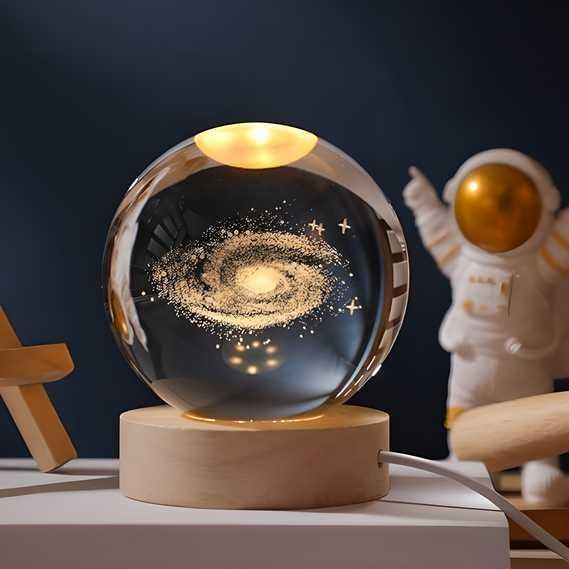 Glass sphere with galaxy design on a wooden base, next to an astronaut figurine.