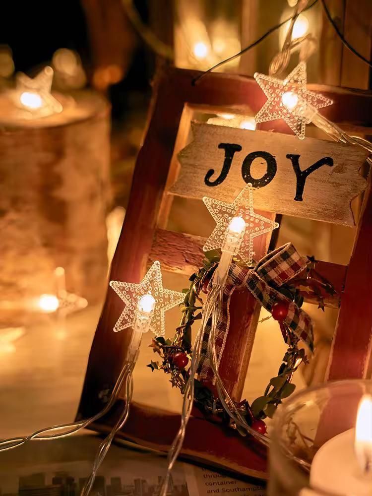 Decorative wooden sign with 'JOY' surrounded by star-shaped lights and candles in the background