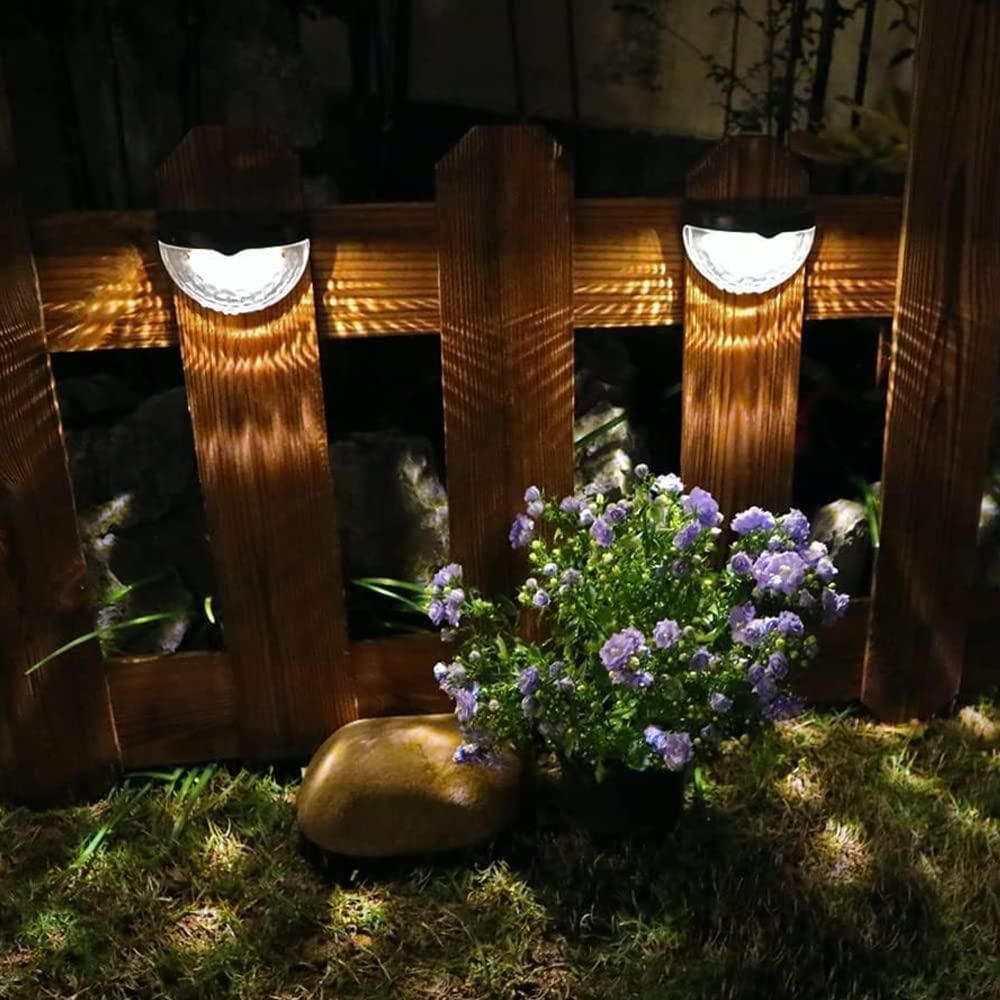 Solar-powered outdoor lights on a wooden fence with flowers and a rock in the foreground.